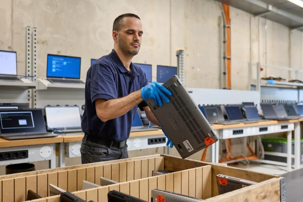 A technician placing a laptop into a crate at a recycling facility