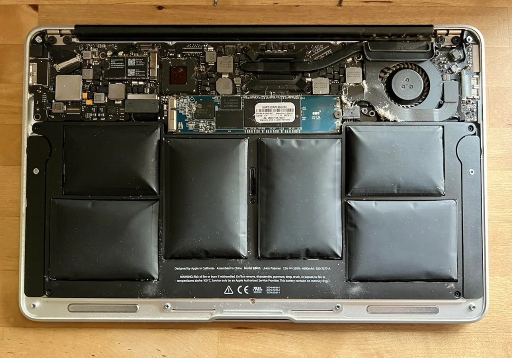 A laptop with its bottom panel bulging outward from swollen battery cells inside